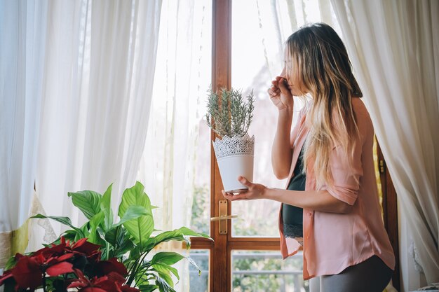 Jonge vrouw zwanger die thuis rozemarijnvaas het ruiken houdt