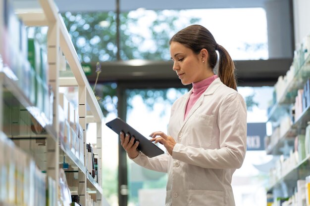 Jonge vrouwelijke apotheker die naar het scherm van een digitale tablet in de apotheek kijkt