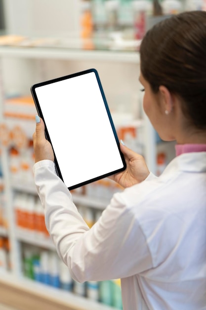 Jonge vrouwelijke apotheker die naar het scherm van een digitale tablet in de apotheek kijkt