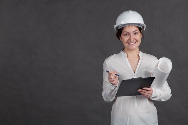 Jonge vrouwelijke architect in een beschermende helm maakt aantekeningen over het project met een papier in handen.