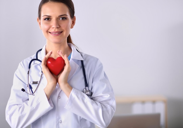 Jonge vrouwelijke arts die een rood hart houdt dat op witte achtergrond wordt geïsoleerd