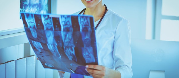 Jonge vrouwelijke arts die met stethoscoop Xray onderzoekt op het kantoor van de dokter