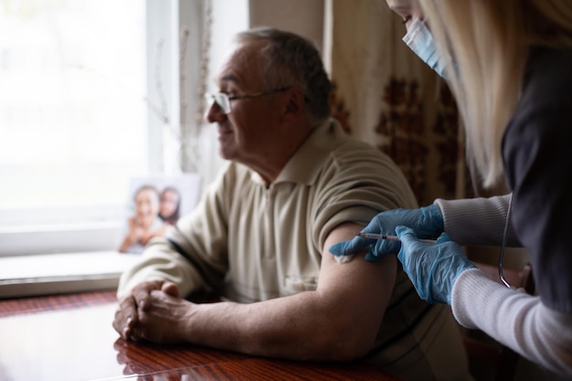 Jonge vrouwelijke arts die vaccin injecteert bij oudere man tijdens huisbezoek.