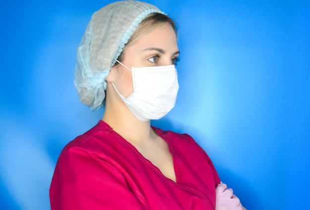 Jonge vrouwelijke arts op een blauwe achtergrond. Gezondheidszorg en geneeskunde concept. Doctor in de witte jas, roze handschoenen en een gezichtsmasker. Pandemisch concept