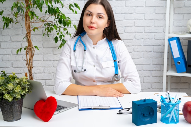 Jonge vrouwelijke artsencardioloog die bij haar bureau en het werken zit