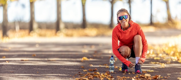 Foto jonge vrouwelijke atleet die schoenveters vastmaakte voordat ze in het herfstpark rende, een fles water leidde haar