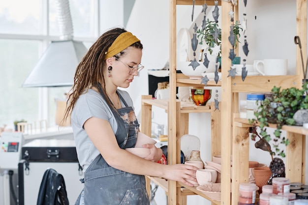 Jonge vrouwelijke bediende van een kleine aardewerk- en souvenirwinkel die bij de presentatie staat