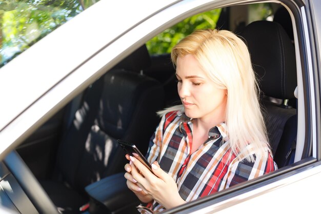 Foto jonge vrouwelijke bestuurder met behulp van touchscreen-smartphone en gps-navigatie in een auto.