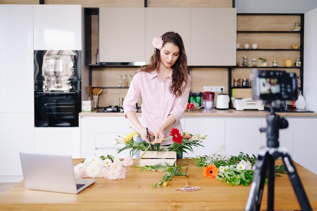 Jonge vrouwelijke bloemist neemt video-tutorial op van bloemencomposities ontwerp op camera vrouw interieurontwerper schiet vlog op camera regel handgemaakte huisbloemdecoraties