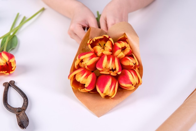 Jonge vrouwelijke bloemist wikkelt een rode kleur tulp bloemboeket voor Moederdag cadeau met stropdas lint strik over een witte tafel achtergrond close-up levensstijl