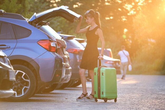 Jonge vrouwelijke chauffeur die de koffer van de bagagekoffer in haar auto laadt. Reizen en vakanties concept