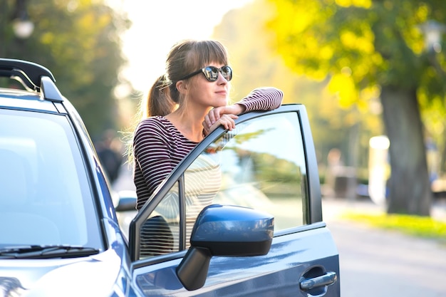 Jonge vrouwelijke chauffeur die in de buurt van haar auto rust en geniet van een warme zomerdag Reis- en uitjeconcept