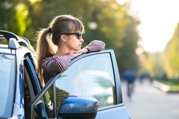 Jonge vrouwelijke chauffeur geniet van een warme zomerdag naast haar auto op straat in de stad. Reizen en vakantie concept.