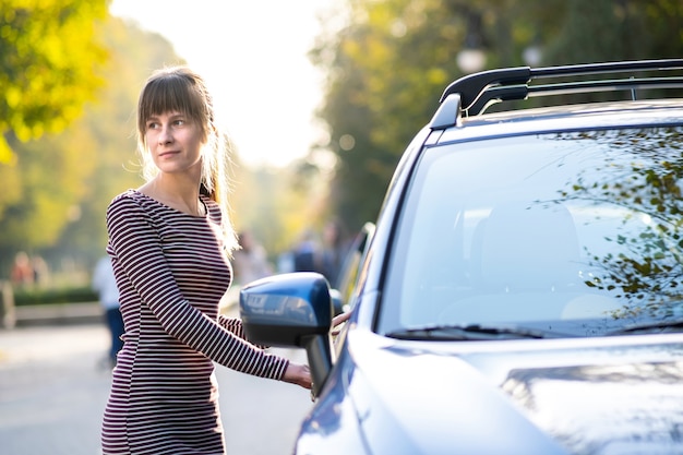 Jonge vrouwelijke chauffeur rust in de buurt van haar auto genieten van warme zomerdag. Reizen en uitje concept.