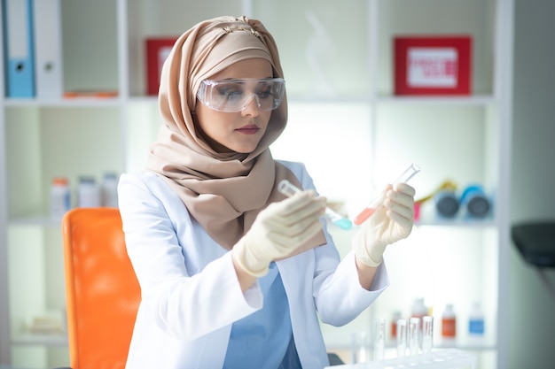 Jonge vrouwelijke chemicus. Jonge vrouwelijke scheikundige hoofddoek en het dragen van witte handschoenen met reageerbuizen