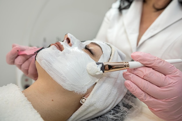 Jonge vrouwelijke cliënt krijgt gezichtsbehandeling van wit masker in beauty spa salon Concept van huidverzorging