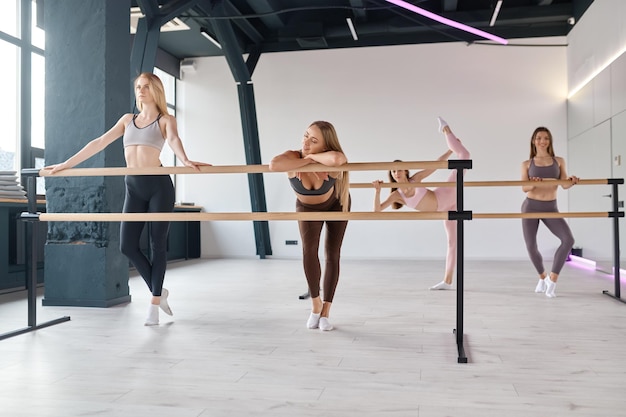 Jonge vrouwelijke dansers die hun benen strekken en balletbewegingen oefenen aan de barre