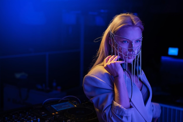 Jonge vrouwelijke DJ in een nachtclub op de console het meisje draagt een wit pak en sieraden op haar gezicht