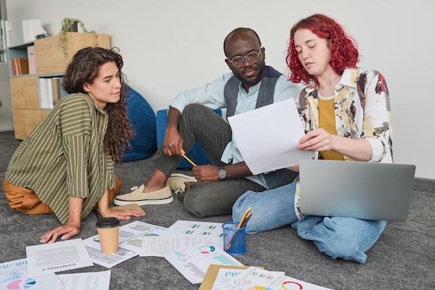 Foto jonge vrouwelijke econoom die gegevens in financieel document uitlegt aan collega's