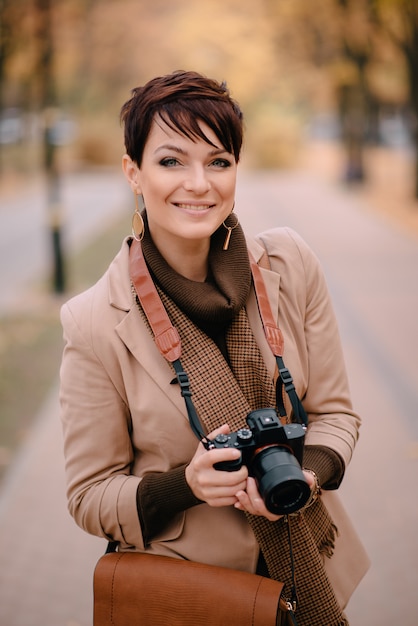 Jonge vrouwelijke fotograaf die camera en het glimlachen bekijkt