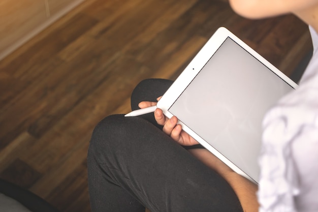 Jonge vrouwelijke freelancer die tablet-pc met wit scherm vasthoudt met de styluspen in de hand, achtergrondfoto van appartement