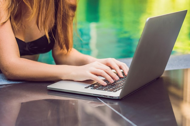 Jonge vrouwelijke freelancer zit bij het zwembad met haar laptop. Druk op vakantie. Verre werk concept. Kopieer ruimte voor uw tekst