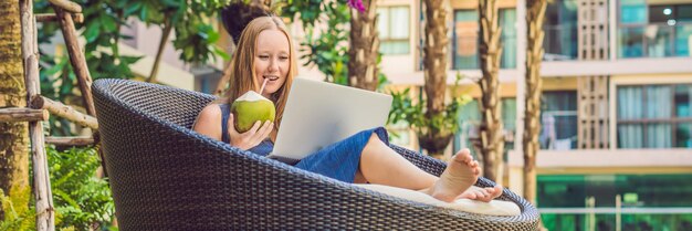 Jonge vrouwelijke freelancer zit bij het zwembad met haar laptop in het hotel en bladert in haar