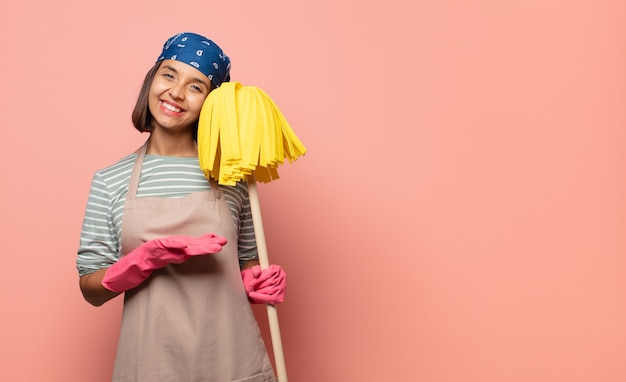 Foto jonge vrouwelijke huishoudster die vrolijk glimlacht, zich gelukkig voelt en een concept toont in kopieerruimte met handpalm