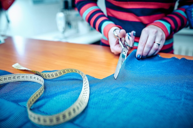 Jonge vrouwelijke modeontwerper die een rode stof snijdt met accessoires voor kleermakerij op tafel