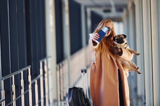 Jonge vrouwelijke passagier in warme kleren wandelen met haar hond in de luchthavenhal.