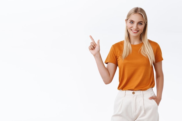 Jonge vrouwelijke professionele aanwijskaart. aantrekkelijk blond meisje met blauwe ogen, tatoeages, hand in hand in broek zorgeloos, linker bovenhoek tonen, vreugdevol glimlachen, advies geven, met vermelding van promo