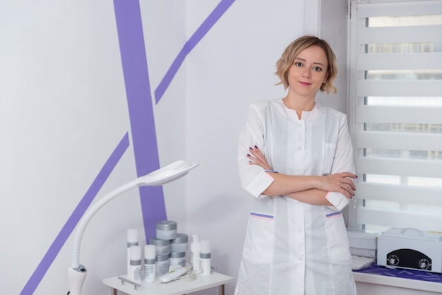 Foto jonge vrouwelijke professionele arts kijkt direct in de camera de cosmetologis in een schoonheidssalon