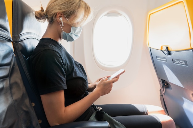 Jonge vrouwelijke reiziger die een preventiemasker draagt tijdens een vlucht in een vliegtuig