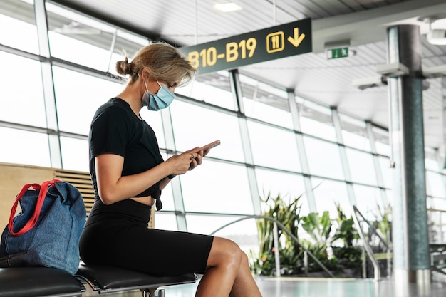 Jonge vrouwelijke reiziger draagt een preventiemasker op een luchthaven tijdens het wachten op de vlucht