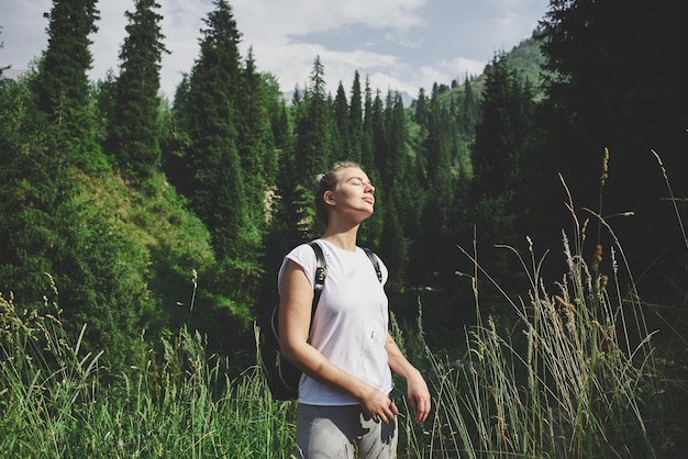 Jonge vrouwelijke reiziger met een rugzak achter haar rug in Zailiysky Alatau in Almaty kijkt naar het berglandschap van de zomer van Kazachstan en geniet van de natuur