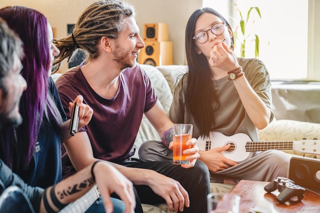 Jonge vrouwelijke rokende joint met cannabis terwijl ze thuis met vrienden op muziekinstrumenten speelt