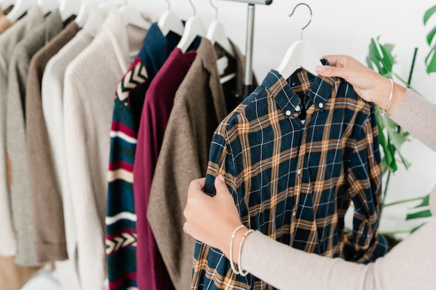 Jonge vrouwelijke shopper hanger met geruit overhemd te houden tijdens het kiezen van nieuwe casual kleding in boetiek