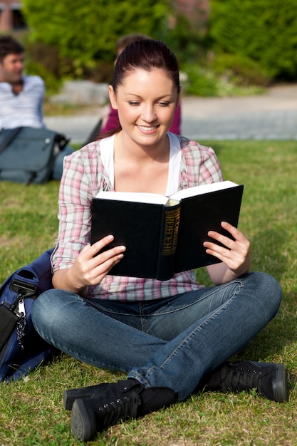Foto jonge vrouwelijke student die een boekzitting op gras leest