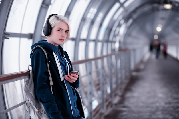 Jonge vrouwelijke student die naar muziek luistert in grote koptelefoons in de metrotunnel