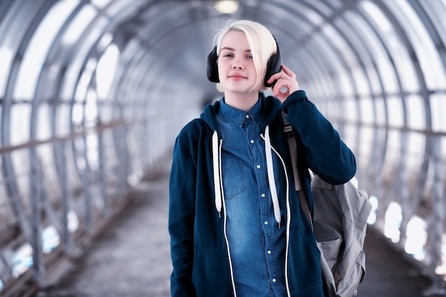 Jonge vrouwelijke student die naar muziek luistert in grote koptelefoons in de metrotunnel