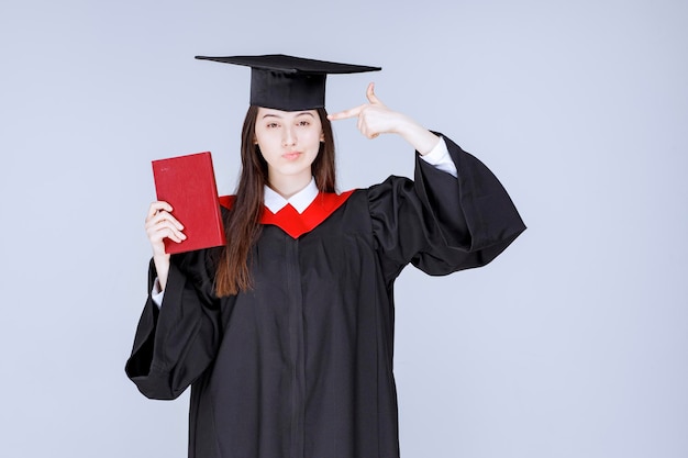 Jonge vrouwelijke student in academische toga wijzend op haar hoofd. Hoge kwaliteit foto