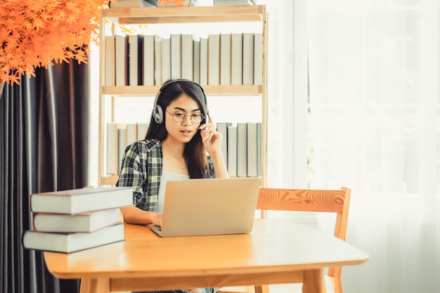 Jonge vrouwelijke student in geruit hemd zittend aan tafel met laptop tijdens het studeren.