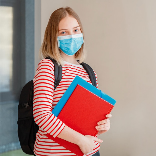 Jonge vrouwelijke student met beschermend medisch masker. Portret van blonde vrouwelijke student Girl aan het interieur van de universiteit tijdens coronavirus covid 19 lockdown.