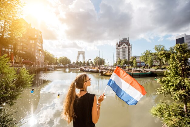 Jonge vrouwelijke toerist die achteruit staat met Nederlandse vlag in de oude haven in de stad Rotterdam