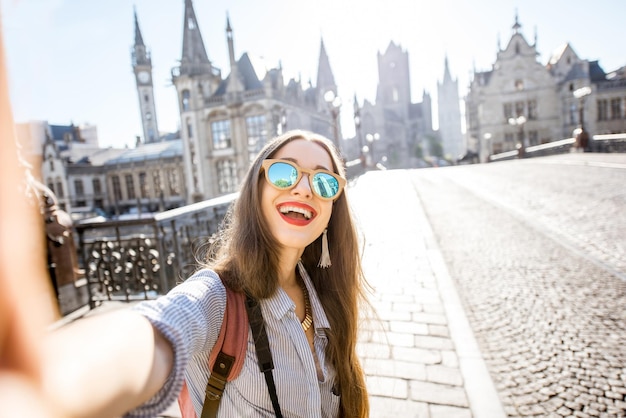 Jonge vrouwelijke toerist die een selfie-foto maakt die op de brug staat met een prachtig uitzicht op de stad Gent in België