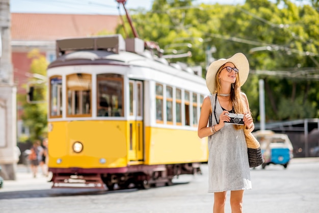 Jonge vrouwelijke toerist die zich dichtbij de beroemde retro gele tram bevindt die in de stad van Lissabon, Portugal reist