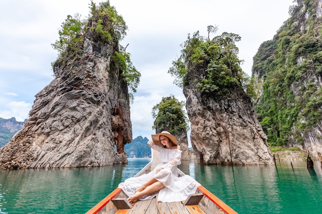 Jonge vrouwelijke toerist in jurk en hoed op Longtail Boat in de buurt van beroemde drie rotsen met kalkstenen kliffen bij Cheow Lan Lake. Reizen vrouw zittend op boot in Khao Sok National Park in Thailand