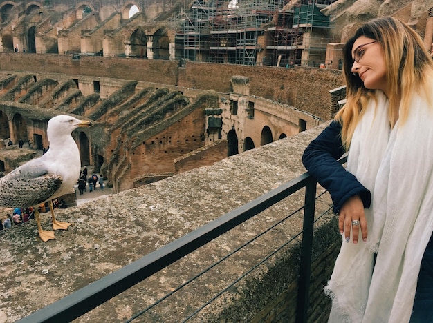 Jonge vrouwelijke toerist kijkt naar een meeuw die op de steunmuur van het Colosseum zit