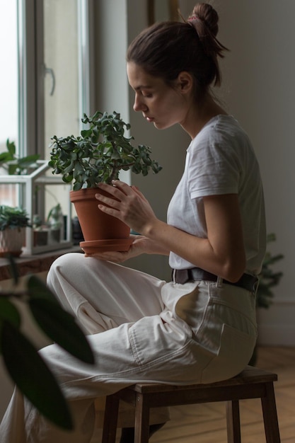Jonge vrouwelijke tuinier die voor een groene huisplant in een pot zorgt tuinieren thuis liefde voor huisplanten