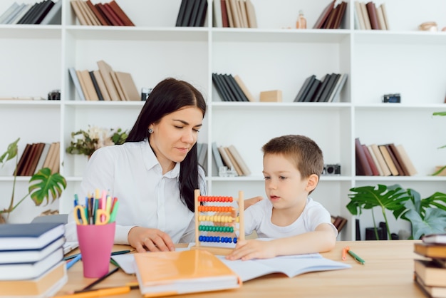 Jonge vrouwelijke tutor die kleine basisschooljongen helpt met huiswerk tijdens individuele les thuis